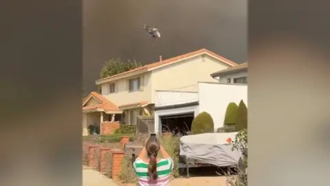 Woman taking picture of a helicopter and wildfire smoke filling the sky