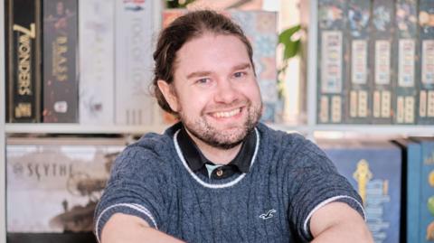 Kari, who has long brown hair tied back and is wearing a grey knitted jumper, smiles 