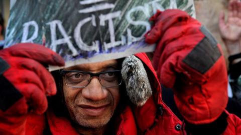 An anti-Trump protestor holds a sign saying "Racism"