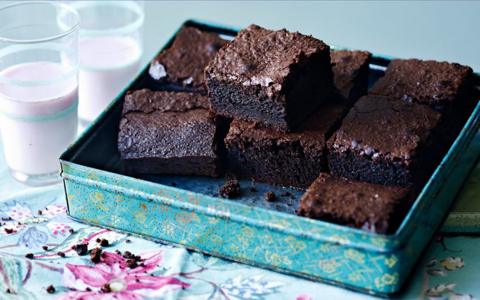 Home made brownies in a tin with glasses of milk to the left