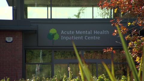 Red brick building with grey sign reading 'Acute Mental Health Inpatient Centre'