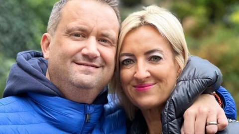 Nick Bowkett with his arm around his wife Pippa, with both looking at the camera and smiling 