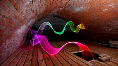 A trail of rainbow light in the right hand corner starting with yellow into, green, blue, purple, pink then into red . The trail of light leads from the top of the image into a hatch in a fishing hut. The fishing hut has a brick arch roof and a wooden floor.