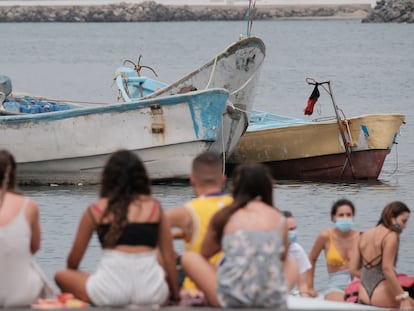 Bañistas frente a los cayucos amontonados en el muelle de Arguineguín, en Gran Canaria, donde han llegado a pernoctar bajo carpas más de 400 inmigrantes.