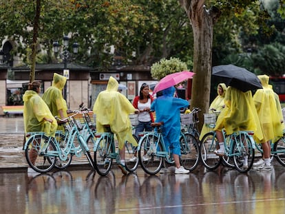 Un grupo de turistas en bicicleta cubiertos con chubasqueros escuchan las indicaciones de su guía este jueves en la plaza del Ayuntamiento de Valencia.