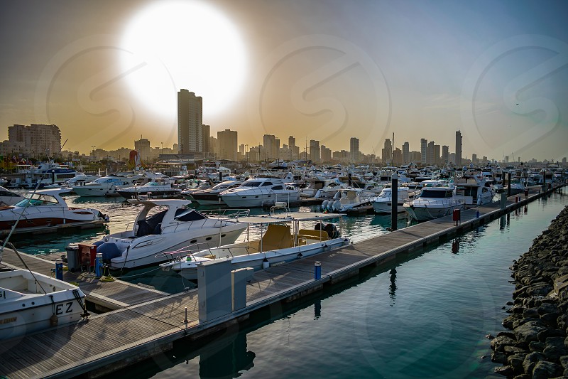 big sun setting over a kuwait marina. many boats and the city in the ...