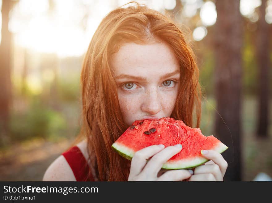 Happy young redhair woman eating watermelon on the nature. Youth lifestyle. Happiness, joy, holiday, beach, summer concept