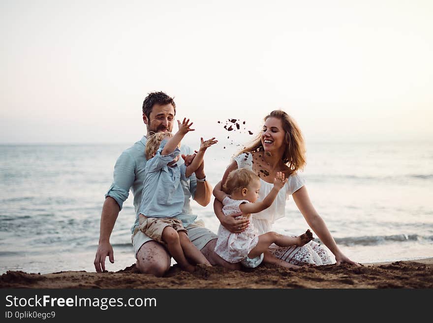 A family with two toddler children sitting on sand beach on summer holiday, playing.