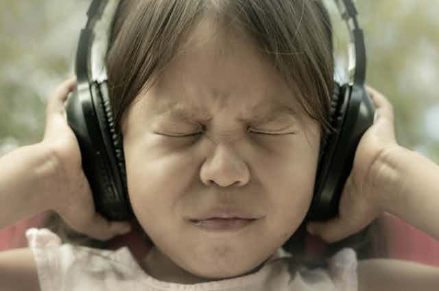 girl shuts eyes tightly and pushes headphones against ears