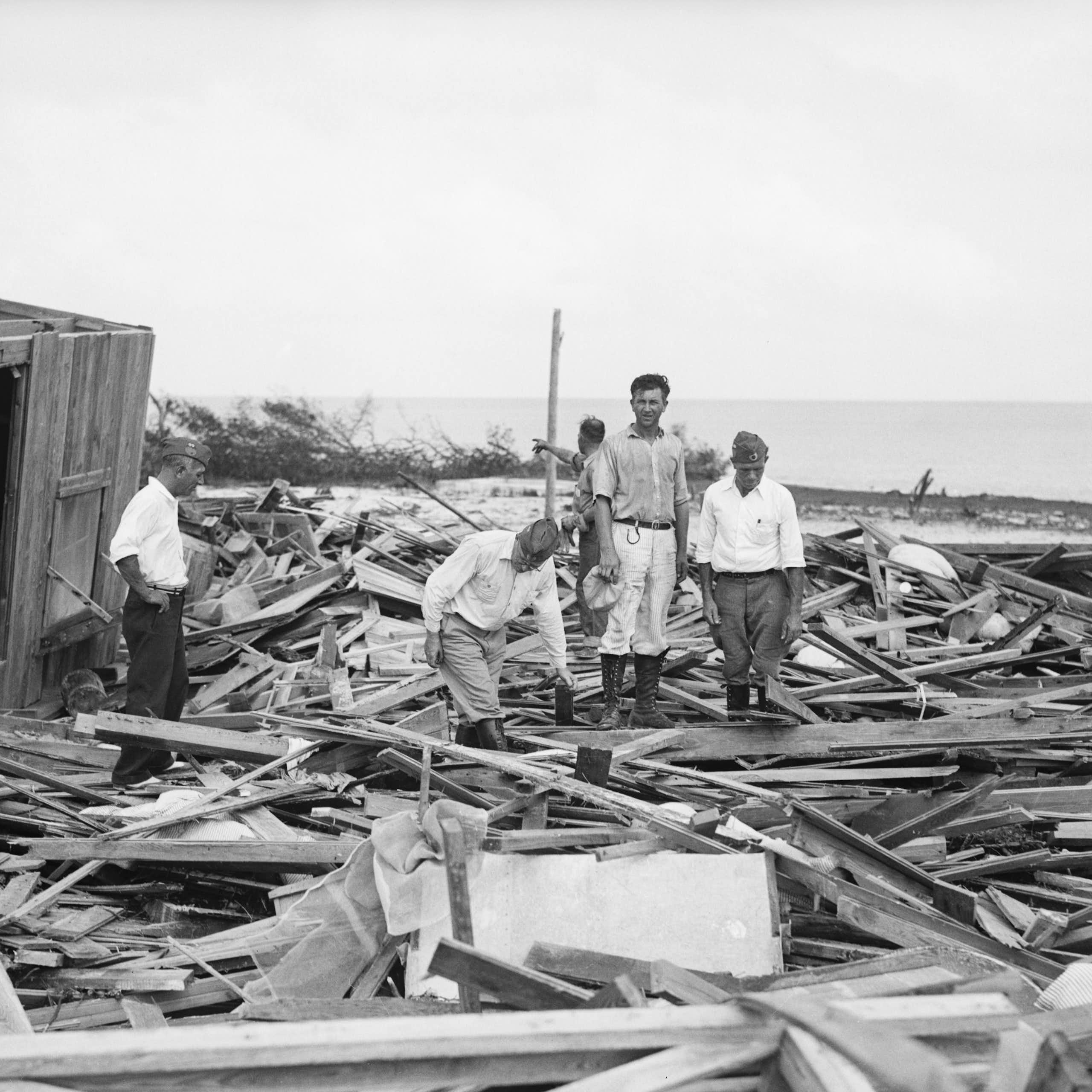 Black and white photo of people standing on debris.