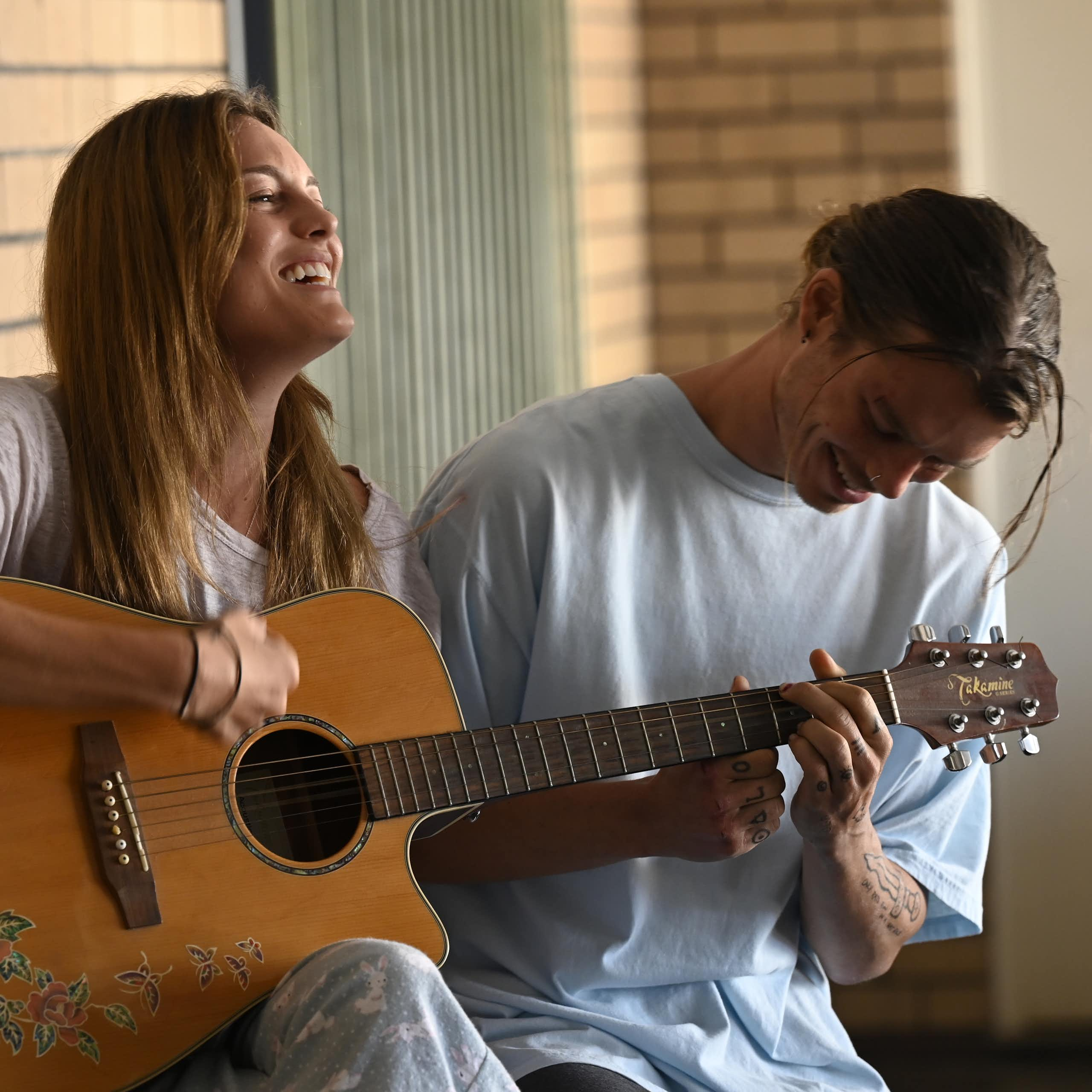 Young woman and man sitting playing a guitar together