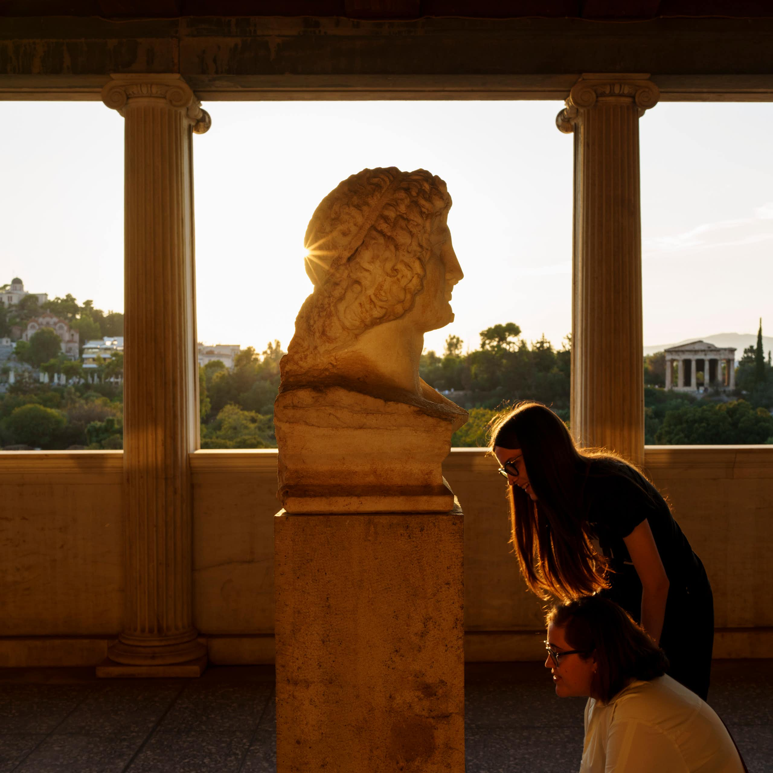 Tourists look at the 2nd century AD bust of Alexander the Great or Eubouleus, a minor Greek deity, at the Museum of the ancient Agora, Stoa of Attalos, with the temple of Hephaestus in the background, in Athens.