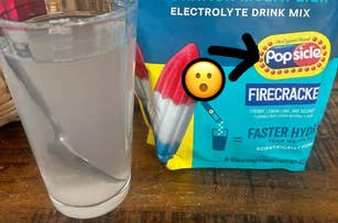 Popsicle Firecracker electrolyte drink mix package sits next to a glass of the mixed drink, with a spoon inside the glass