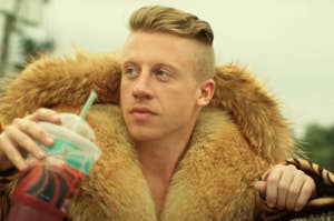 Macklemore wearing a fur jacket, holding a drink while looking to the side in the Thrift Shop music video