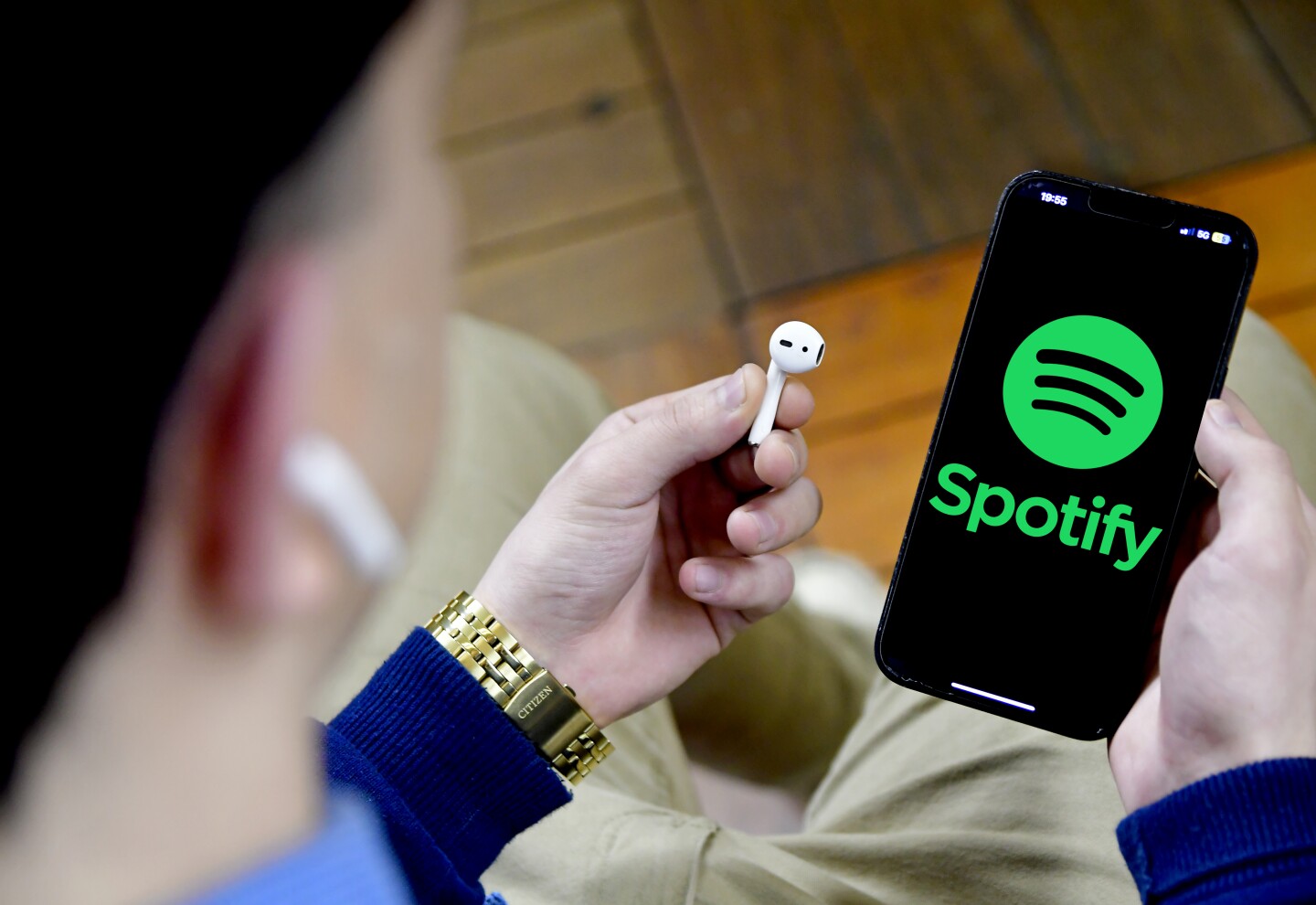 Una persona con un celular con la aplicación de Spotify y auriculares inalámbricos.