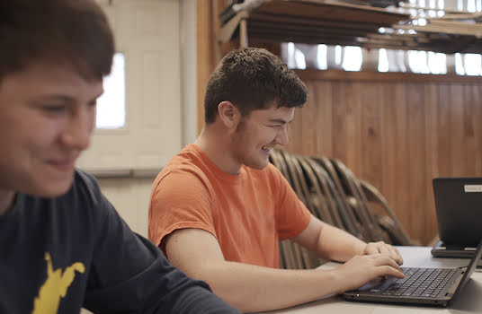 Two teenage boys working on computers and laughing.