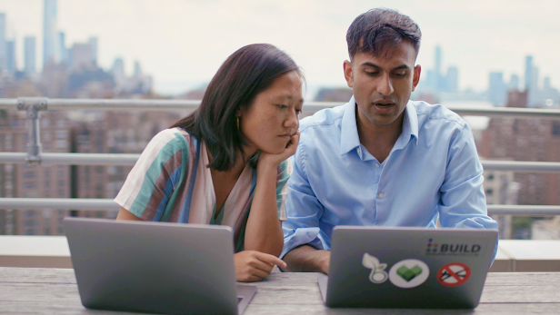 A man and woman sit at a table and work on laptops together