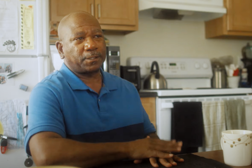 Black man at his kitchen table, smiles at camera