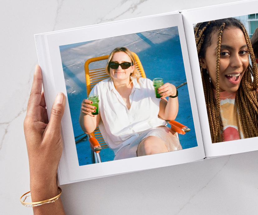 Hands holding a photo book opened to a page featuring a woman holding two drinks in a beach chair.