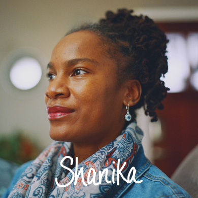 Black woman with natural hair wearing earrings and a patterned scarf smiling into the distance