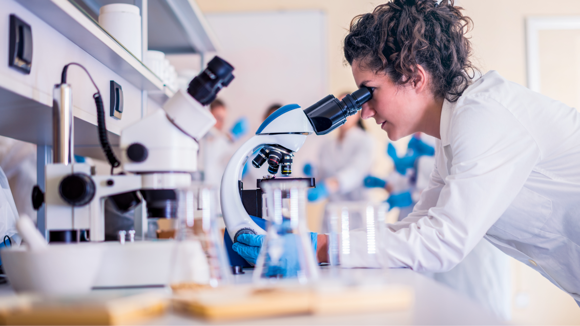 A scientist looking into a microscope in a lab. 