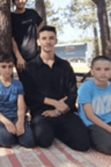 a group of young boys are sitting on a blanket under a tree .