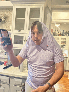 a man wearing a hooded shirt is holding a cell phone in front of a kitchen with a sign that says bib