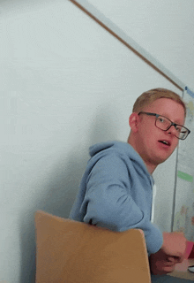 a man wearing glasses is sitting in front of a whiteboard