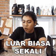 a woman is sitting at a counter with a cup of coffee and the words luar biasa sekali written on her face