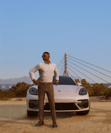 a man stands in front of a white porsche with a bridge in the background