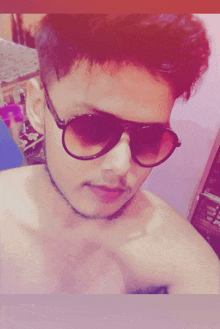 a shirtless young man wearing sunglasses takes a selfie