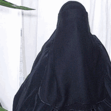 a woman wearing a black veil is standing in front of a window