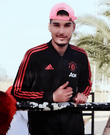 a young man wearing an adidas jacket and a pink hat stands next to a railing