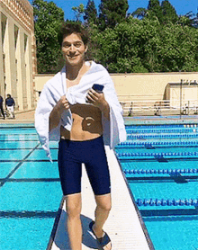 a man with a towel wrapped around his shoulders is standing on a diving board in front of a swimming pool