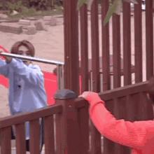 a man in a blue shirt is standing next to a woman in a red sweater behind a wooden fence .