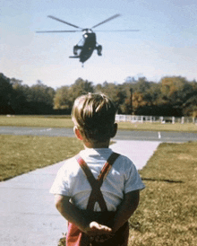 a young boy stands in front of a helicopter flying in the sky