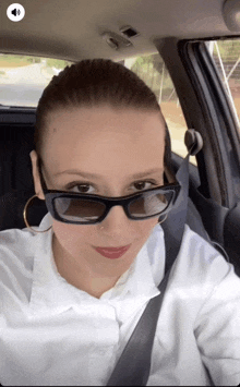 a woman in a car wearing sunglasses and a white shirt