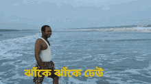 a man in a white tank top is standing in the water on a beach with a foreign language written on the bottom