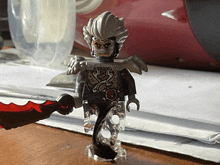 a lego figure holding a red sword on a wooden table