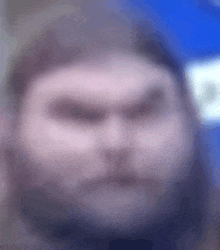 a blurry picture of a man 's face with a beard and a serious look on his face .