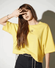 a woman in a yellow t-shirt and black jeans is covering her face with her hand .