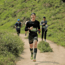 a runner with a green number on his shirt is running on a dirt path