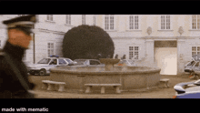 a police officer stands in front of a fountain in front of a building with cars parked in front of it