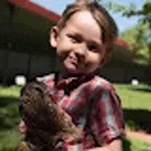 a young girl in a plaid shirt is holding a small animal in her hands .