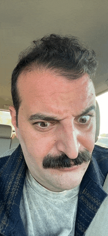 a man with a mustache making a funny face in a car