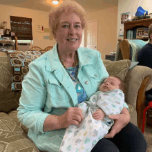 a woman in a blue jacket is holding a baby in her lap