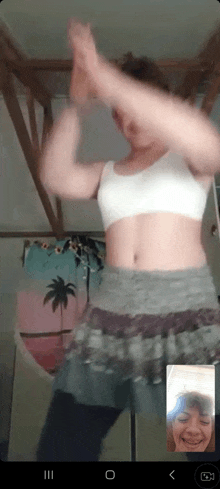 a woman in a crop top and skirt is dancing on a video call with another woman .