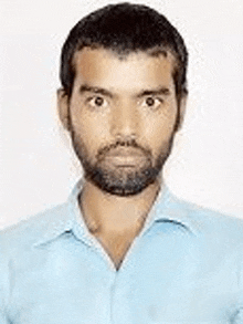 a man with a beard is wearing a light blue shirt and looking at the camera .