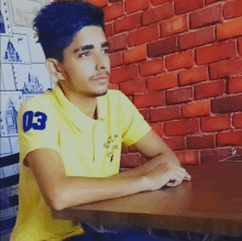 a young man wearing a yellow shirt with the number 03 on the sleeve sits at a table