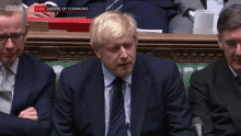 a man in a suit and tie is sitting in front of a microphone with bbc live on the screen behind him